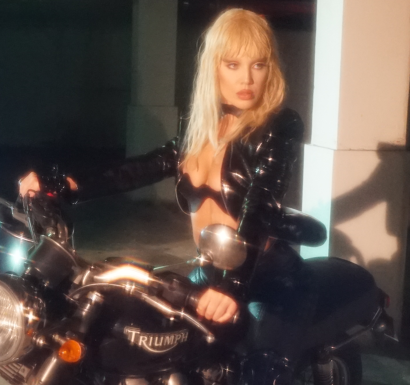 A low fi photo of singer Sam Quealy sittign astride a Triumph motorcycle at night