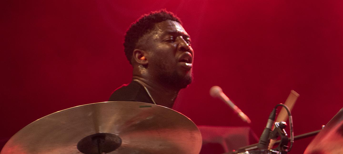 Femi Koleoso plays the drums on a stage that is lit red.