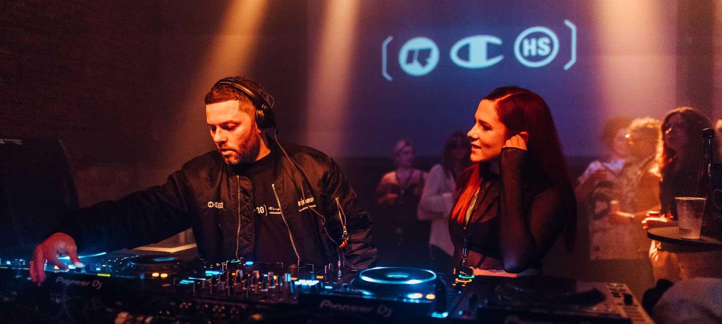 Rinse FM founder Geeneus on the decks with a guest to his right and a crowded audience in the background at a 30th anniversary event