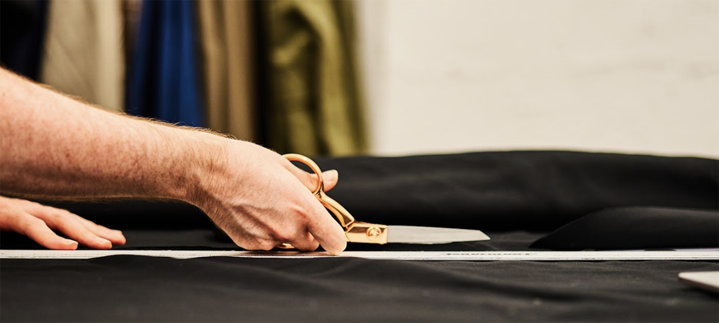 A hand holds a pair of scissors cutting a piece of fabric.