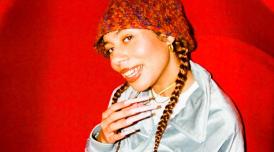 A portrait of DJ and singer Ella Knight in a textured bucket hat, sitting in a red chair