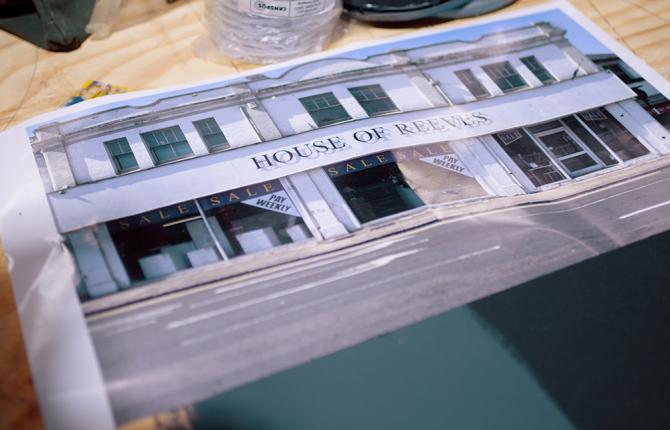 A photo of the furniture shop House of Reeves lays on a desk, surrounded by paint stains, a stanley knife and bottle of white spirits.